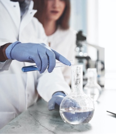 Hand pouring chemical over a flask.