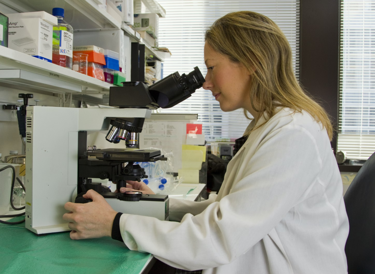 A lab person looking into a microscope.