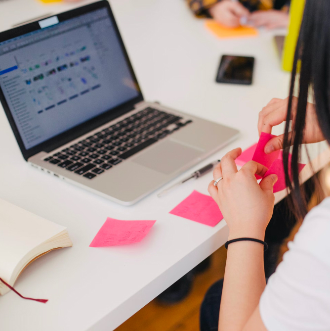 Woman jotting down notes on her pink sticky notes.