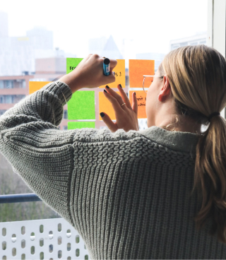 Woman writing down notes onto sticky notes placed on a window.
